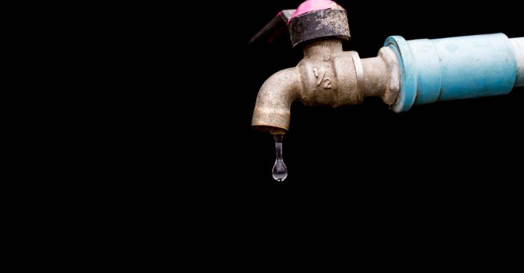 a detailed view of a metal faucet with a single water drop against a black background