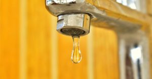 a close up shot of a water droplet hanging from a stainless steel faucet highlighting surface tensi